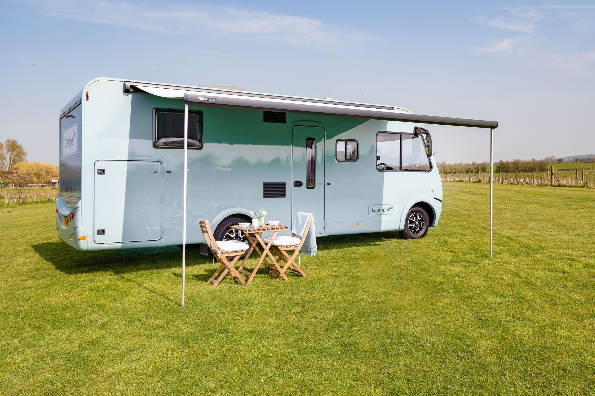 GlamperRV luxury motorhome with awning and outdoor dining set on a green field